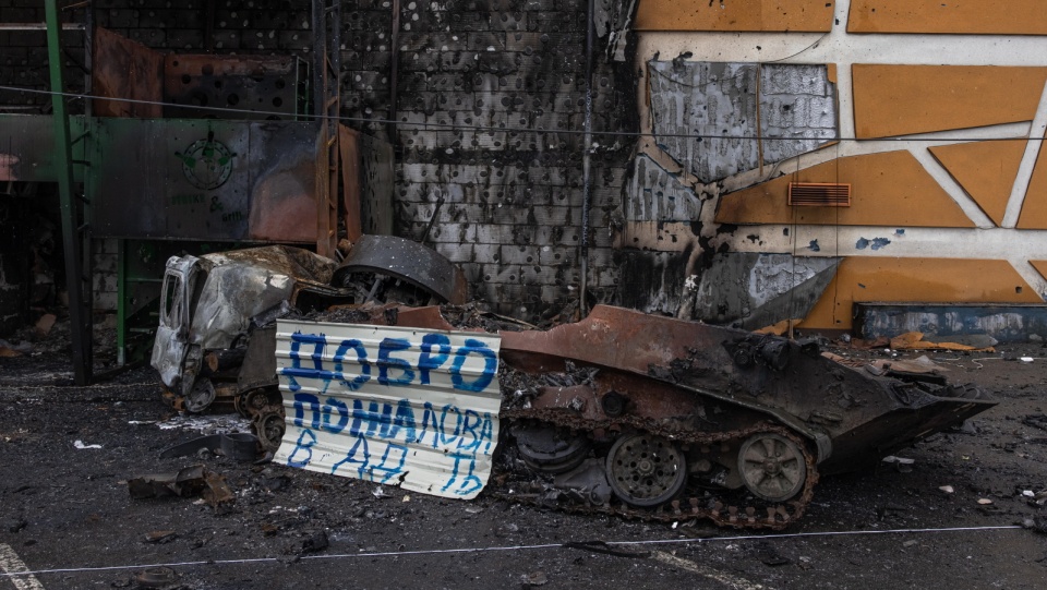 Metalowa tabliczka z napisem „Witamy w piekle” obok zniszczonego po walkach rosyjskiego pojazdu wojskowego, w mieście Irpin w obwodzie kijowskim. Fot. PAP/EPA/RZYMSKI PILIPEJ